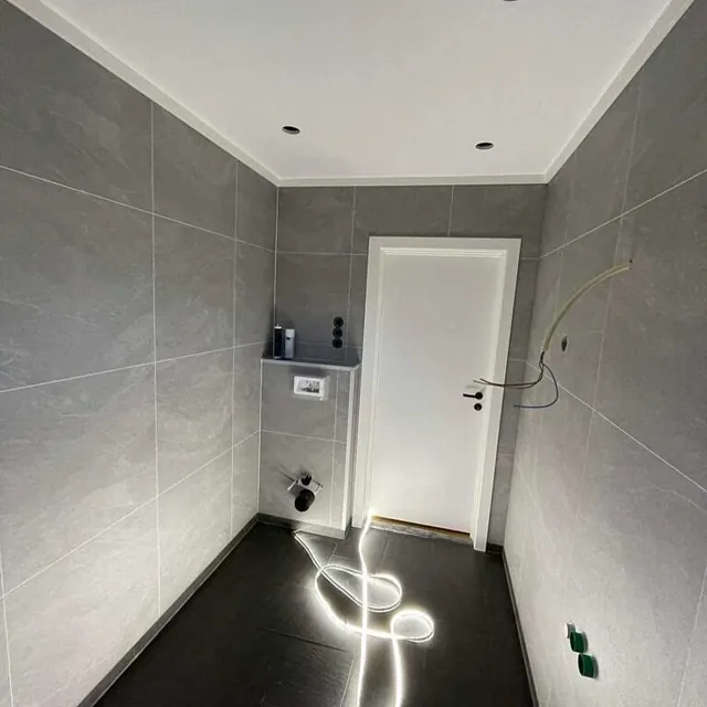 Smal gang med grå vegger, downlights og hvit dør.